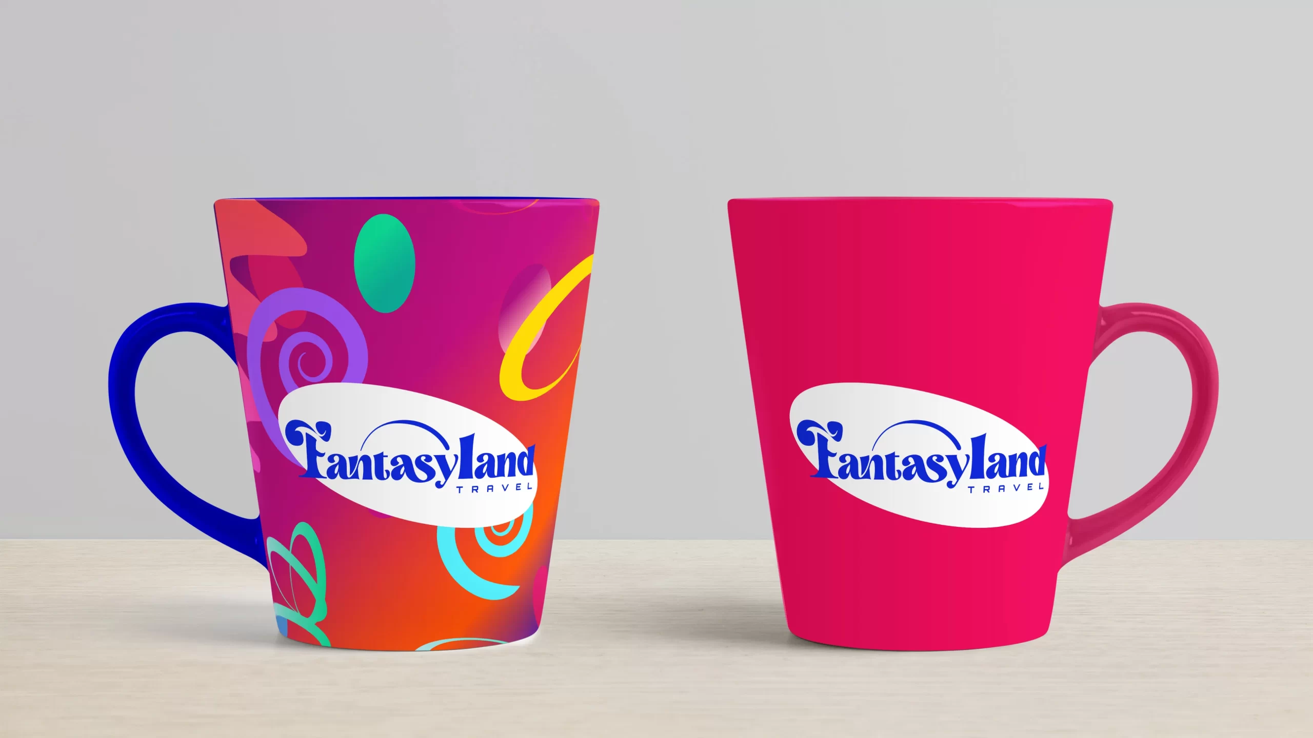 duas canecas com logotipo da Fantasyland Travel, a da esquerda é colorida com asa azul e a da diretia é rosa sobre uma mesa e uma parede cinza ao fundo